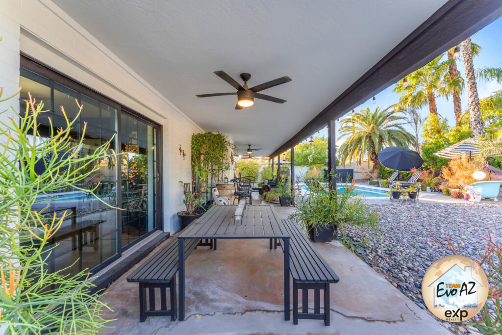 Covered patio seating area with ceiling fan and landscaped yard